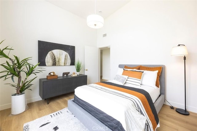 bedroom featuring baseboards, visible vents, a towering ceiling, and wood finished floors