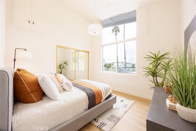 bedroom with baseboards, light wood-style floors, a closet, and a towering ceiling