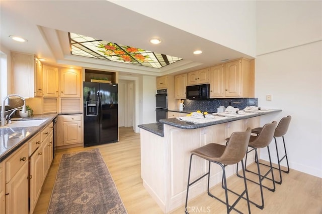 kitchen with a sink, a raised ceiling, light brown cabinets, and black appliances