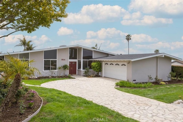 mid-century modern home with stucco siding, a garage, a front lawn, and decorative driveway