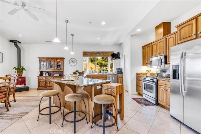 kitchen featuring brown cabinets, a wood stove, light tile patterned floors, light stone countertops, and appliances with stainless steel finishes
