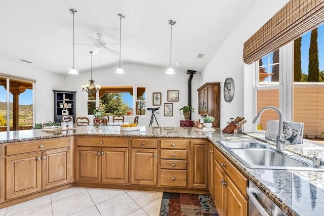 kitchen with brown cabinets, ceiling fan with notable chandelier, a sink, vaulted ceiling, and light stone counters