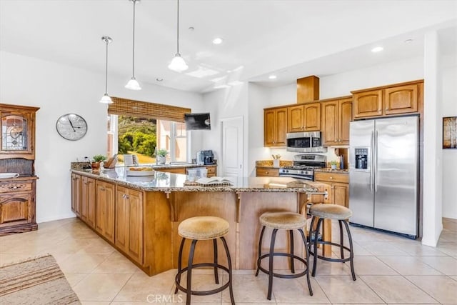 kitchen featuring light stone countertops, a breakfast bar area, a peninsula, brown cabinets, and appliances with stainless steel finishes