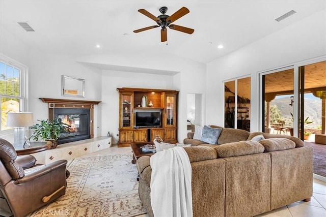 living room featuring light tile patterned floors, ceiling fan, a glass covered fireplace, and visible vents