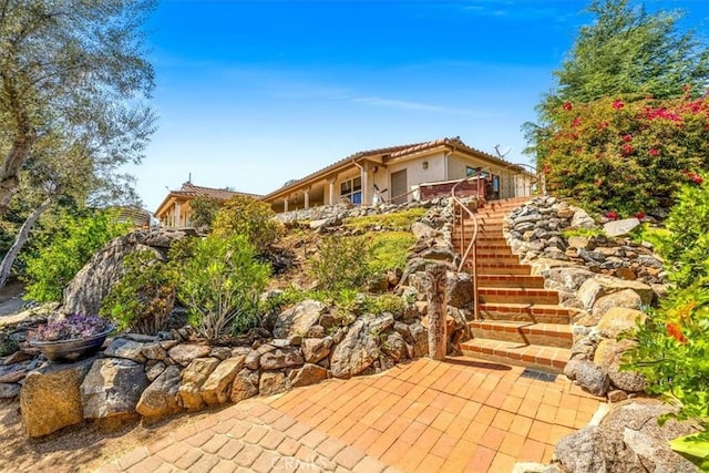 exterior space with a tile roof, stucco siding, and stairway