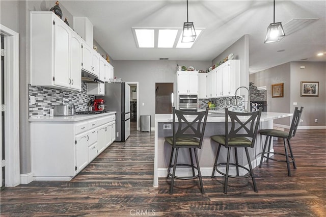 6748 Coriander Dr, Oak Hills, CA 92344 - kitchen with a kitchen breakfast bar, under cabinet range hood, backsplash, dark wood-style floors, and appliances with stainless steel finishes
