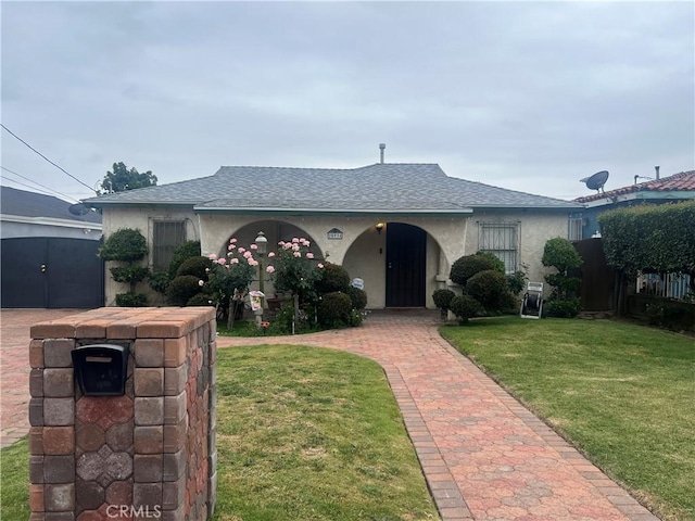 ranch-style house featuring a shingled roof, stucco siding, fence, and a front yard
