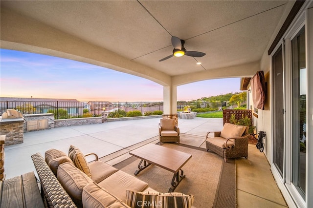 patio terrace at dusk featuring exterior kitchen, an outdoor living space, a fenced backyard, and ceiling fan