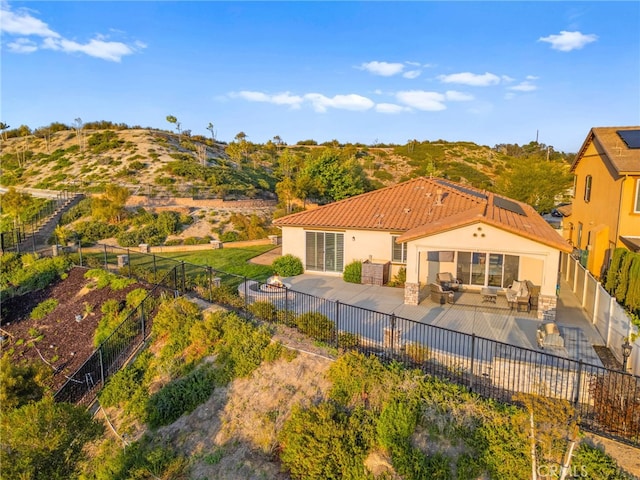 rear view of property featuring a tiled roof, an outdoor living space with a fire pit, a fenced backyard, and roof mounted solar panels