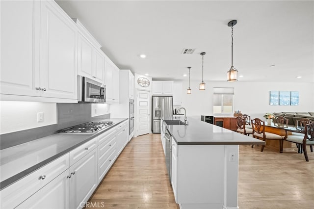 kitchen with appliances with stainless steel finishes, a sink, light wood-type flooring, recessed lighting, and white cabinetry