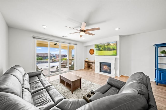 living area with ceiling fan, light wood-style flooring, a glass covered fireplace, and baseboards