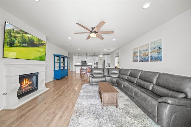 living area featuring a ceiling fan, recessed lighting, light wood-type flooring, a glass covered fireplace, and baseboards