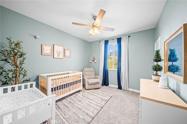 bedroom featuring light colored carpet, baseboards, a crib, and a ceiling fan