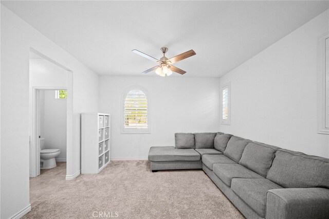 living area featuring light colored carpet, ceiling fan, and baseboards
