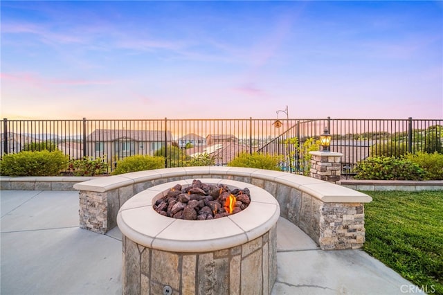 patio terrace at dusk featuring an outdoor fire pit and fence