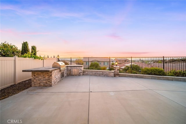 patio terrace at dusk featuring exterior kitchen, a fenced backyard, and grilling area
