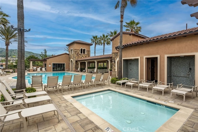 back of property with a community pool, a mountain view, a patio, stucco siding, and a tiled roof