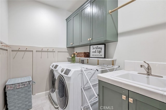 laundry area with washing machine and dryer, a sink, cabinet space, a decorative wall, and wainscoting