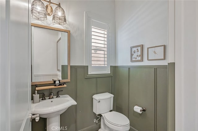 half bath with toilet, a decorative wall, and wainscoting