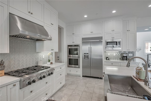 kitchen with a sink, built in appliances, under cabinet range hood, decorative backsplash, and white cabinets