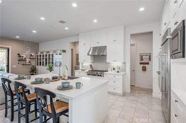 kitchen featuring a sink, a breakfast bar, visible vents, an island with sink, and range hood