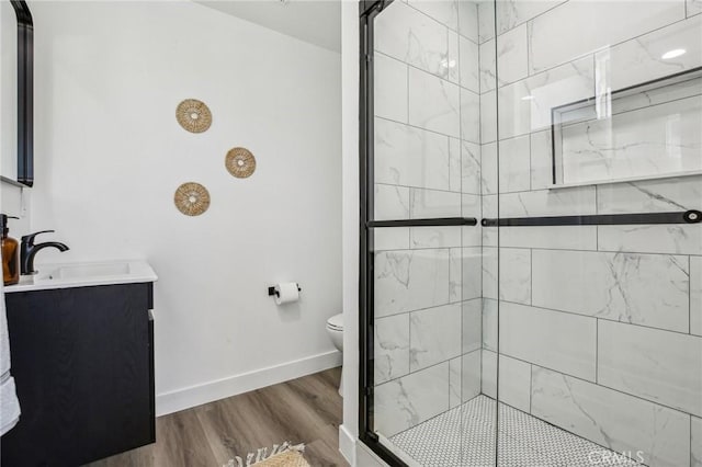 full bathroom with toilet, wood finished floors, tiled shower, baseboards, and vanity