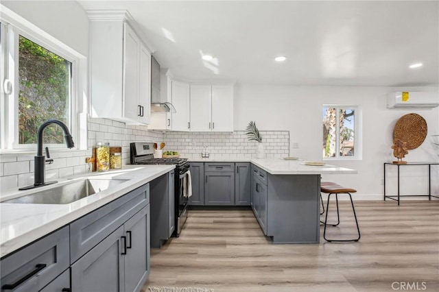 kitchen with a peninsula, a sink, gray cabinets, gas range, and a wall mounted AC