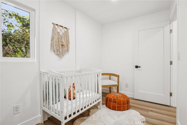 bedroom featuring baseboards, a crib, and wood finished floors