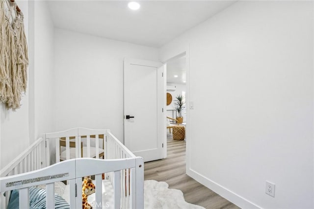 bedroom with baseboards, a nursery area, recessed lighting, and wood finished floors