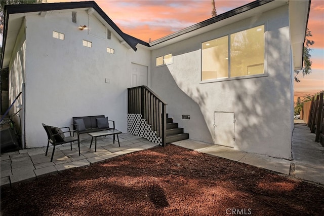 back of house at dusk with fence, stucco siding, and a patio area