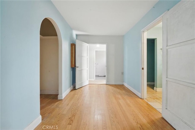hall with arched walkways, baseboards, and light wood-type flooring