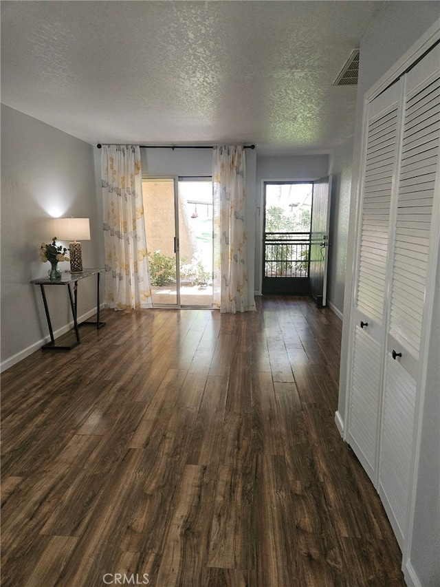 spare room featuring a textured ceiling, visible vents, baseboards, and dark wood-style floors