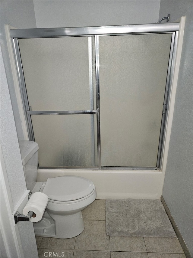 bathroom featuring combined bath / shower with glass door, toilet, and tile patterned floors