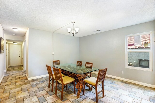 9387 Hot Springs Rd, Corona, CA 92883 - dining room featuring a notable chandelier, stone tile flooring, a textured ceiling, visible vents, and baseboards