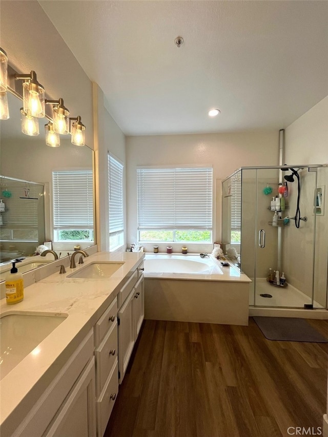 full bath featuring a sink, wood finished floors, a shower stall, double vanity, and a garden tub