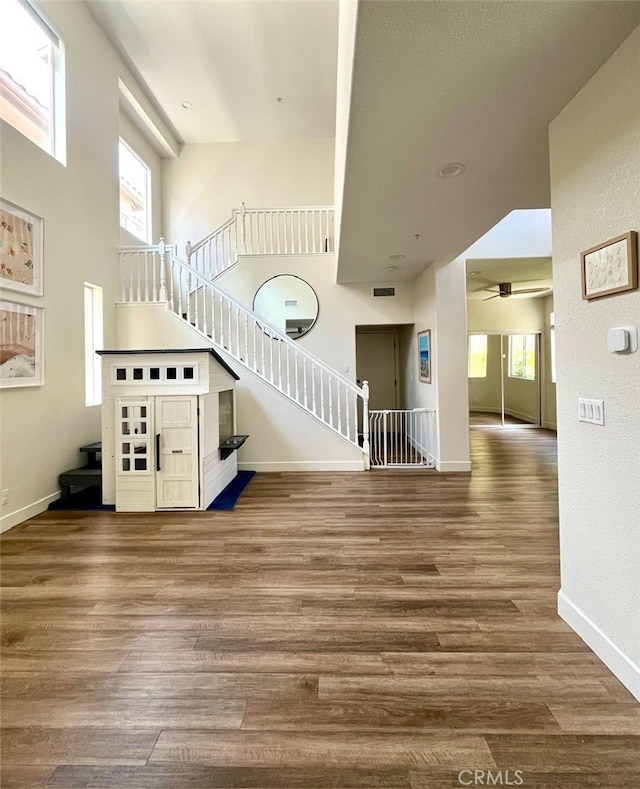 unfurnished living room with wood finished floors, baseboards, a towering ceiling, ceiling fan, and stairs
