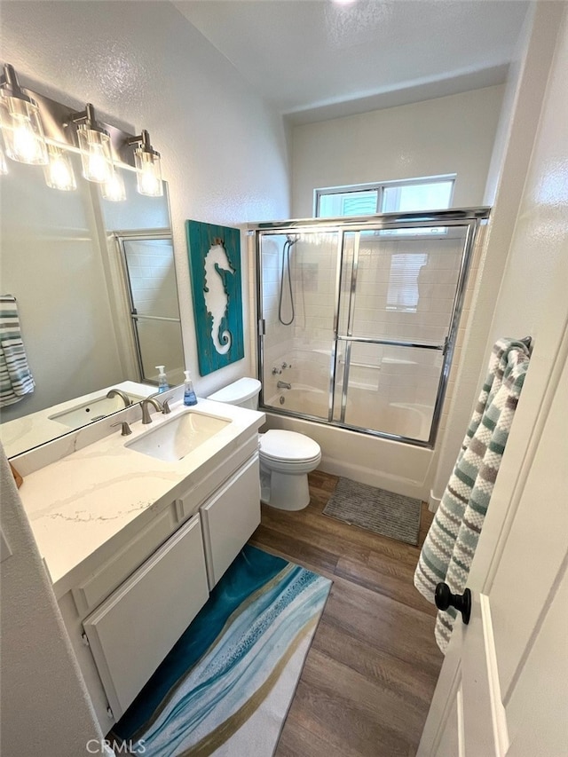 bathroom featuring enclosed tub / shower combo, vanity, toilet, and wood finished floors