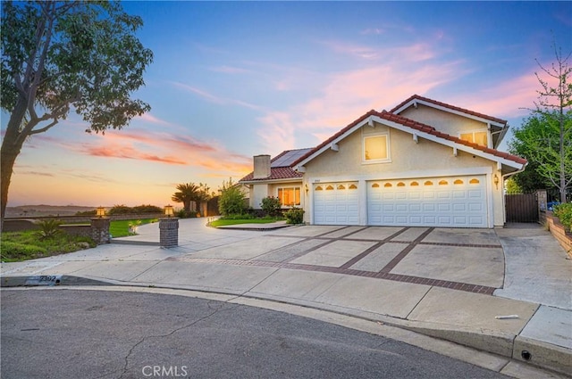 traditional-style home featuring roof mounted solar panels, stucco siding, driveway, and a tiled roof