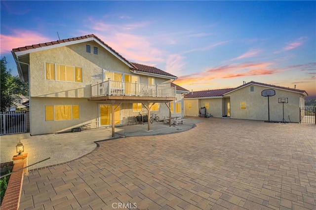 back of property at dusk featuring fence, a patio, stucco siding, and a deck