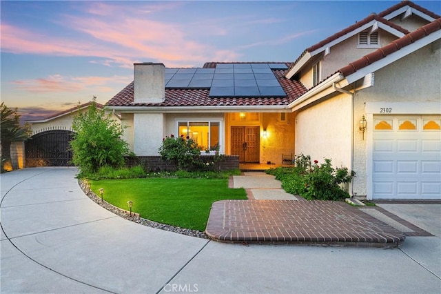 view of front of home featuring a tiled roof, solar panels, stucco siding, a front yard, and a gate