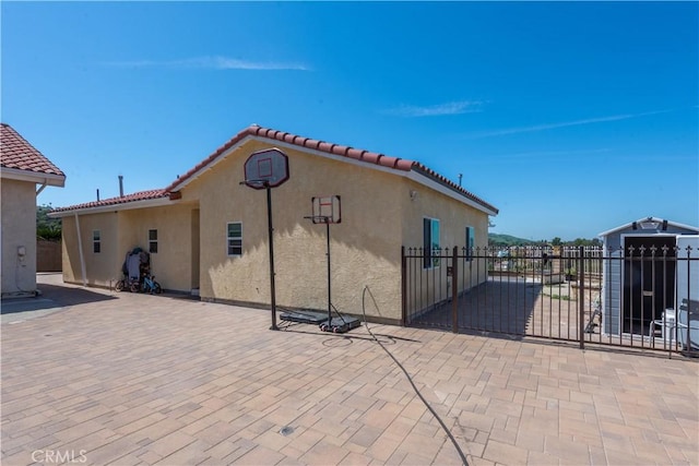 rear view of property with stucco siding, a tiled roof, fence, and a gate