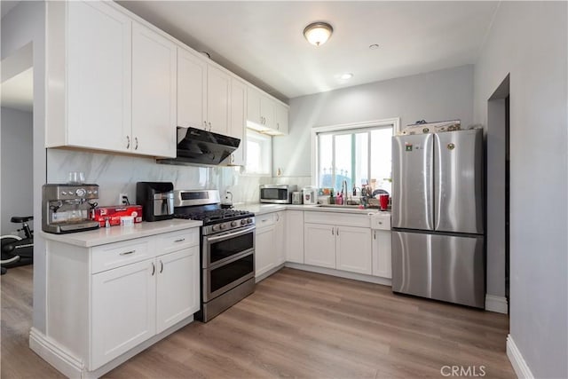 kitchen featuring under cabinet range hood, white cabinetry, light countertops, and appliances with stainless steel finishes