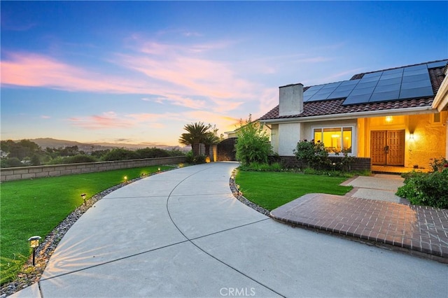 view of front of property featuring a front lawn, roof mounted solar panels, stucco siding, and a tile roof