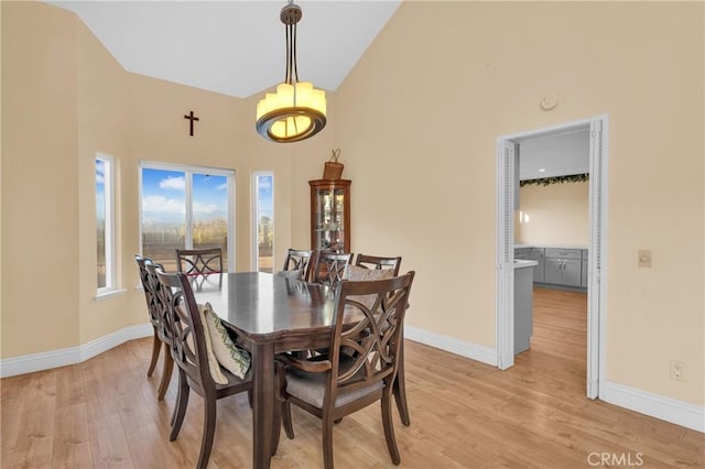 dining room with baseboards, light wood finished floors, and high vaulted ceiling