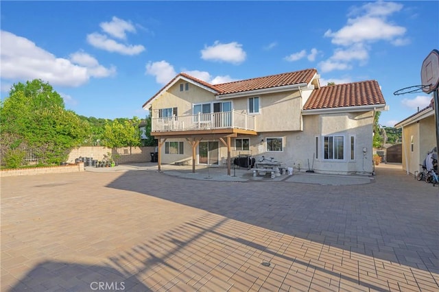 back of house featuring stucco siding, a tile roof, fence, a deck, and a patio area
