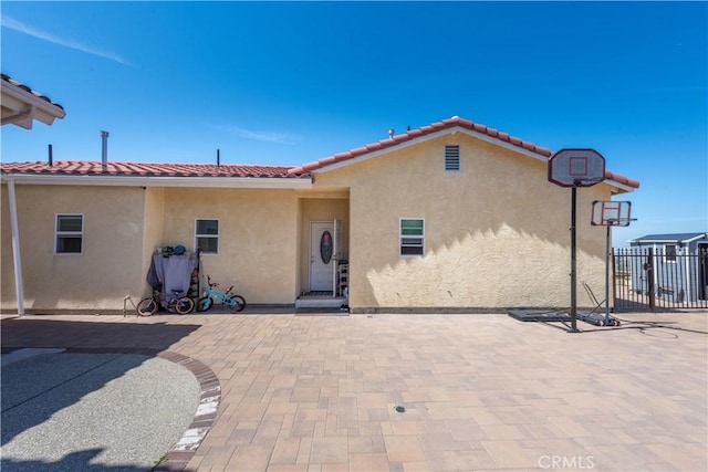 rear view of house with a tiled roof, stucco siding, and fence
