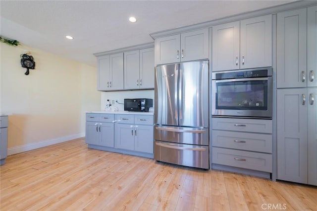 kitchen featuring recessed lighting, light wood finished floors, gray cabinetry, baseboards, and appliances with stainless steel finishes