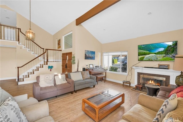 living room with stairs, wood finished floors, high vaulted ceiling, baseboards, and a glass covered fireplace