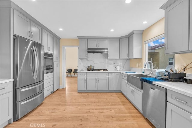 kitchen with a sink, appliances with stainless steel finishes, gray cabinets, light wood-style floors, and tasteful backsplash