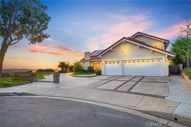 traditional home featuring driveway, stucco siding, a tile roof, and roof mounted solar panels
